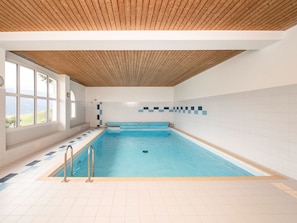 Een zwembad met een houten plafond, betegelde wanden en een uitzicht door grote ramen.