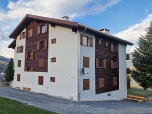 A multi-story residential building with a white facade and wooden accents, featuring multiple windows and a satellite dish.