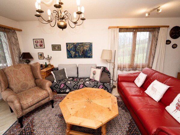 A living room with a patterned sofa, a red leather couch, a wooden coffee table, and a chandelier.