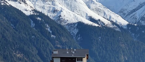 Un bâtiment moderne doté d’un toit plat, entouré de montagnes enneigées et de forêts denses.