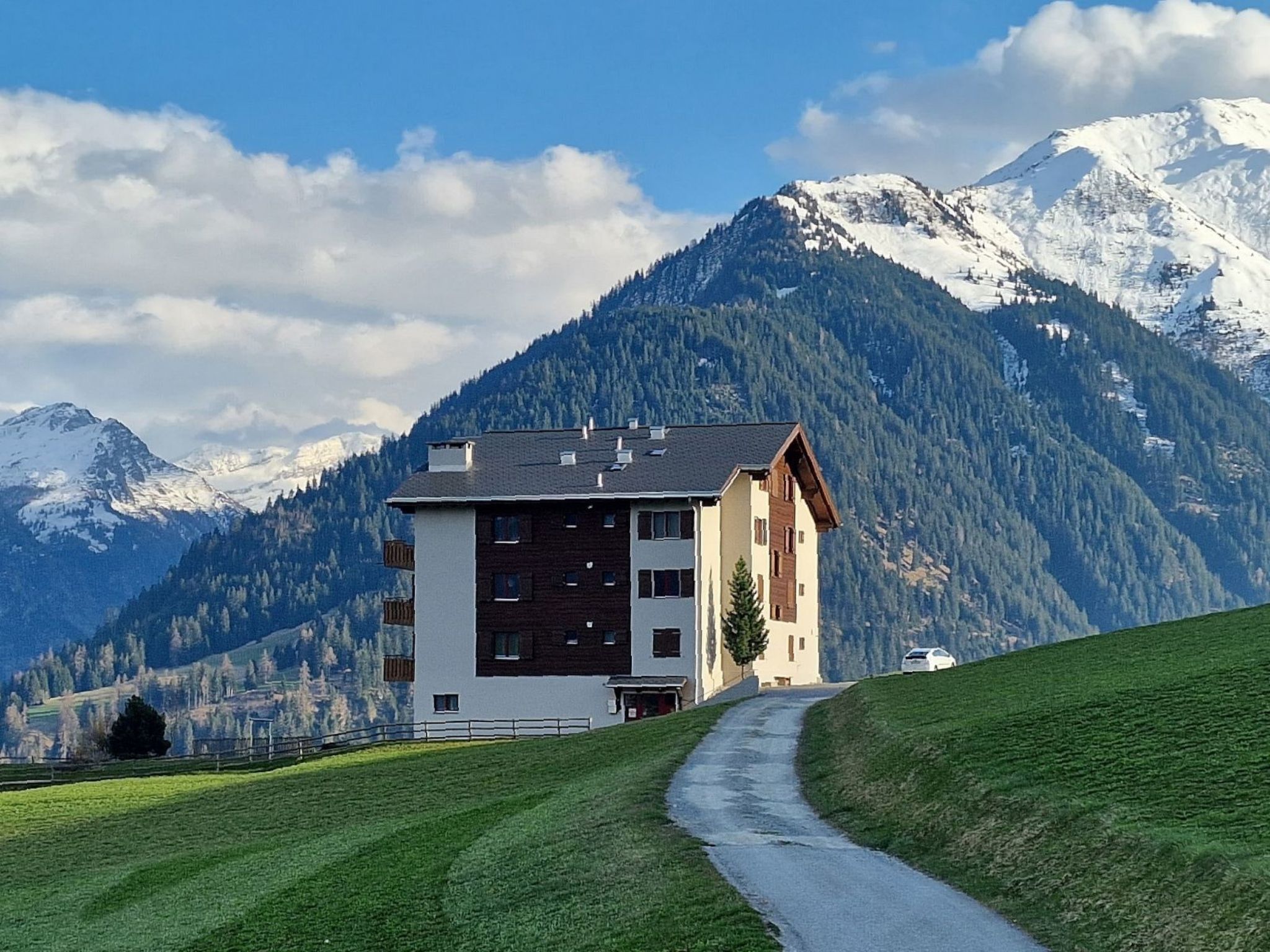 A two-story building with a sloped roof, a pathway leading to it, and snow-capped mountains in the background.