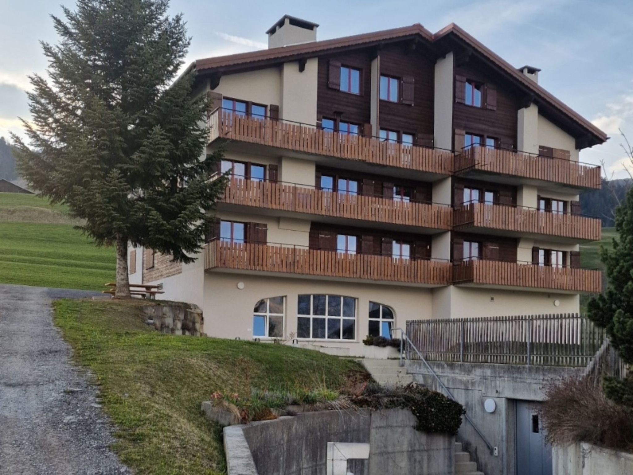 Un edificio de varios pisos con balcones, un acceso cubierto y una zona verde al frente.