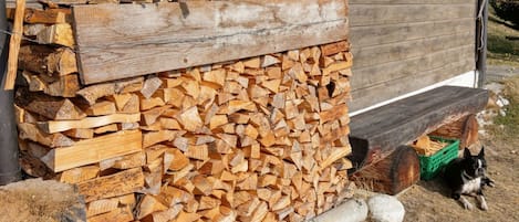 Une pile de bois de chauffage est appuyée contre le mur extérieur d’un bâtiment en bois.