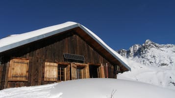 Eine Holzhütte in den Bergen mit geneigtem Dach, einer Holztür und einem Fenster.