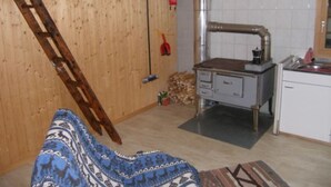 A room with a wooden ceiling, a kitchen area with a stove, and a bed with a patterned blanket. - Tegia Veglia / Erlebnisalp Glivers, Sumvitg, (Sumvitg), 75002B by Interhome (Cumpadials)