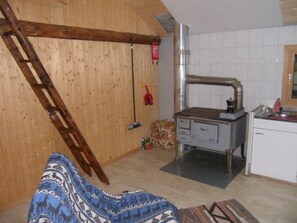 A room with a wooden ceiling, a kitchen area with a stove, and a couch. - Tegia Veglia / Erlebnisalp Glivers, Sumvitg, (Sumvitg), 75002B by Interhome (Cumpadials)