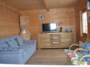 Un interior de cabaña acogedor con un sofá gris, un mueble de madera, un televisor de pantalla plana y mobiliario de mimbre.