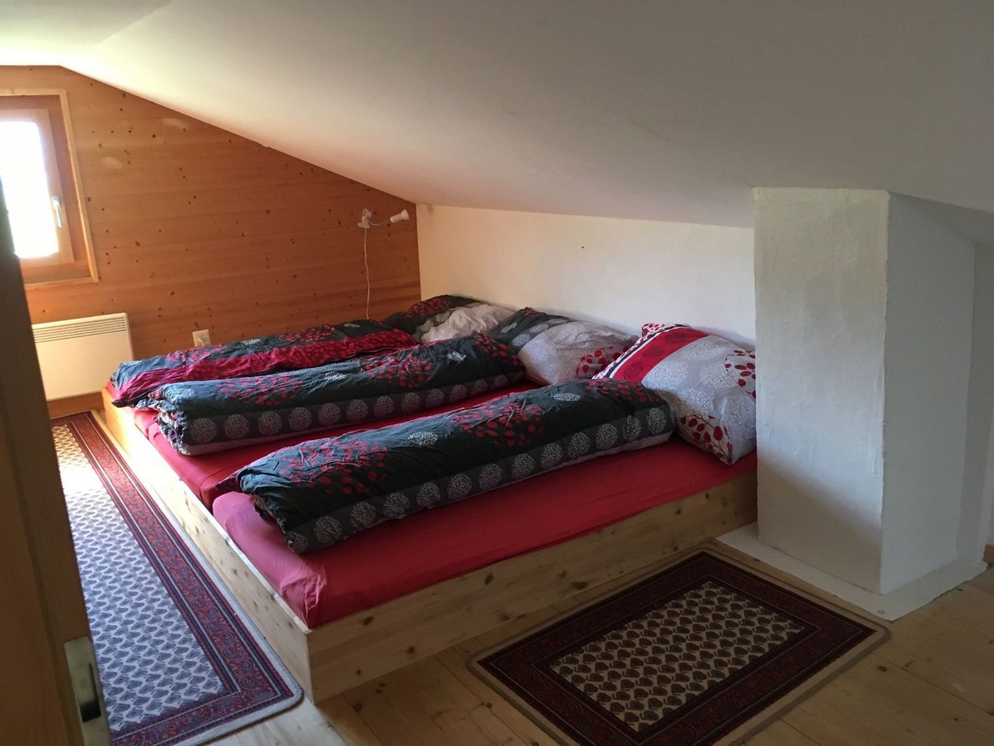 Een kamer met een schuine kap, een bed met een bed met dessin, een radiator en een raam.