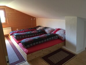 Une pièce avec un plafond en pente, un lit avec une literie à motifs, un radiateur et une fenêtre.