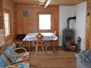 A cozy cabin interior with a wooden interior, a dining table with chairs, a sofa, a fireplace, and a window.