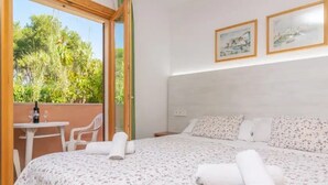 Ein Schlafzimmer mit Bett, kleinem Tisch, zwei Stühlen und einem Balkon mit Blick auf Bäume.