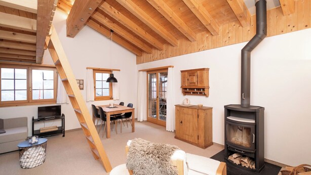 Un amplio espacio tipo loft con techo alto, vigas de madera, chimenea, comedor y escalera.