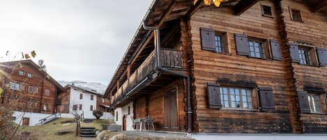 Un chalet traditionnel en bois, doté d’un balcon, d’un chemin en pierre et offrant une vue sur le paysage environnant.