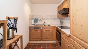 Una cocina compacta con armarios de madera, horno empotrado, un lavabo y una tetera sobre una mesita.