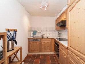 A compact kitchen with wooden cabinets, a built-in oven, a sink, and a kettle on a small table. - Cresta 54, Obersaxen-Misanenga, (Obersaxen), by Interhome (Obersaxen Affeier)