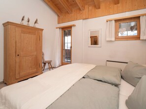 A bedroom with a wooden wardrobe, a bed with grey bedding, a small window with curtains, and a mirror on the wall. - Cresta 54, Obersaxen-Misanenga, (Obersaxen), by Interhome (Obersaxen Affeier)