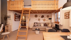 Una habitación estilo loft con una escalera de madera, un sofá, una mesa de comedor y un televisor.