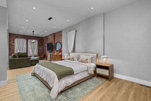 Un dormitorio moderno con una cama grande, un sofá verde, una mesita de noche de madera y una pared de ladrillo.