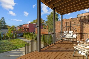 Terraza exterior techada con una mecedora y mobiliario de mimbre, rodeada por un muro de ladrillo y una valla de madera.