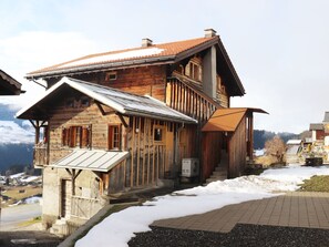 A wooden chalet with a sloped roof, a balcony, and a view of the mountains.
