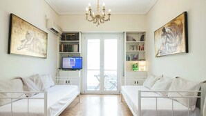 Ein Zimmer mit zwei weißen Betten, einer Kandelaberleuchte, Bücherregalen und Kunstwerken an den Wänden.
