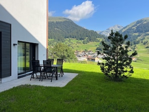 A modern building with a patio area featuring a table and chairs, overlooking a mountainous landscape with a small village in the distance. - Tschuppina Schiess, Brigels, (Breil/Brigels), 65092B by Interhome (Breil/Brigels)