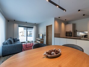 A modern living room with a sofa, a dining table with a decorative bowl, and a kitchen area with appliances. - Tschuppina Schiess, Brigels, (Breil/Brigels), 65092B by Interhome (Breil/Brigels)