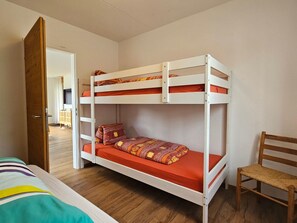 A bunk bed with a lower bunk and a chair, a wooden door, and a hallway leading to another room.