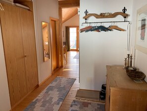 A hallway with wooden flooring, a patterned rug, a wooden dresser with a mirror, and a coat rack with hangers. - Haus Vicasa, Andiast, (Andiast), 59003B by Interhome (Andiast)