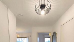 A hallway with a modern ceiling light fixture, a door on the right, and a view into a dining area with natural light. - Sea & Elegance in the 8th district - Prado beaches on foot & garden terrace (Marseille)