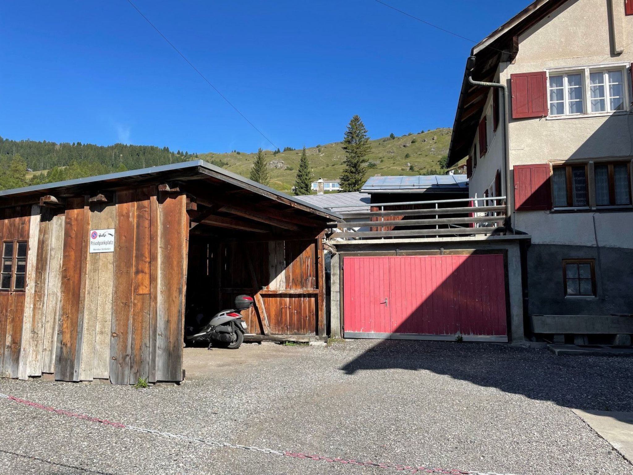 A rustic building with a red garage door, a wooden shed, and a motorcycle parked in front.