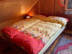 A wooden cabin room with a bed, a red blanket, and a patterned rug.