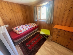 A small, wooden-paneled room with a bed, a small table, and a dresser. - Venini, Rumein, (Degen), 45005B by Interhome (Vattiz)