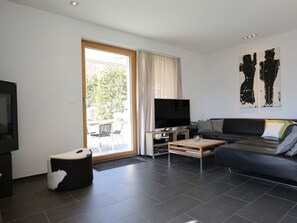 A modern living room with a flat-screen TV, a sofa, a coffee table, and a sliding glass door leading to an outdoor area. - Ferienhaus Davos Munts, Vattiz, (Vattiz), 46012B by Interhome (Vattiz)