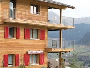 A wooden multi-story building with balconies, red shutters, and a view of a valley. - Vitg Vattiz, Vattiz, (Vattiz), 46002B by Interhome (Vattiz)