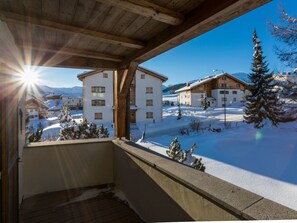 Un balcon en bois offrant une vue sur un paysage enneigé et sur des bâtiments.