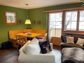 A cozy living room with a wooden dining table, a sofa, and a window with curtains. - Casa Belinda Haht, Brigels, (Breil/Brigels), 65062B by Interhome (Breil/Brigels)