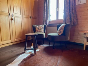 A room with wooden panel walls, two upholstered chairs with patterned cushions, a small stool, and a window with curtains. - Casa Belinda Haht, Brigels, (Breil/Brigels), 65062B by Interhome (Breil/Brigels)