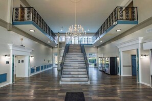 A spacious hotel lobby with a central staircase, a chandelier, and a view of the outdoors. - Sleek- Mins To - Atrium Health & CIA & Stadium (Charlotte)