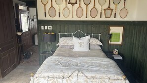 Un dormitorio con una cama, una mesita de noche, una lámpara, un cuadro enmarcado y un soporte en la pared para raquetas de tenis.