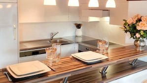 Moderni keittiö, jossa on valkoiset kaapit, puinen työtaso, sisäänrakennettu uuni ja riippuvalaisimet.
