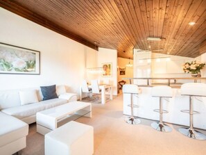 Ein modernes Wohnzimmer mit Holzboden, einem weißen Sofa, einem Couchtisch und einer Küchenzeile mit Barhocker.