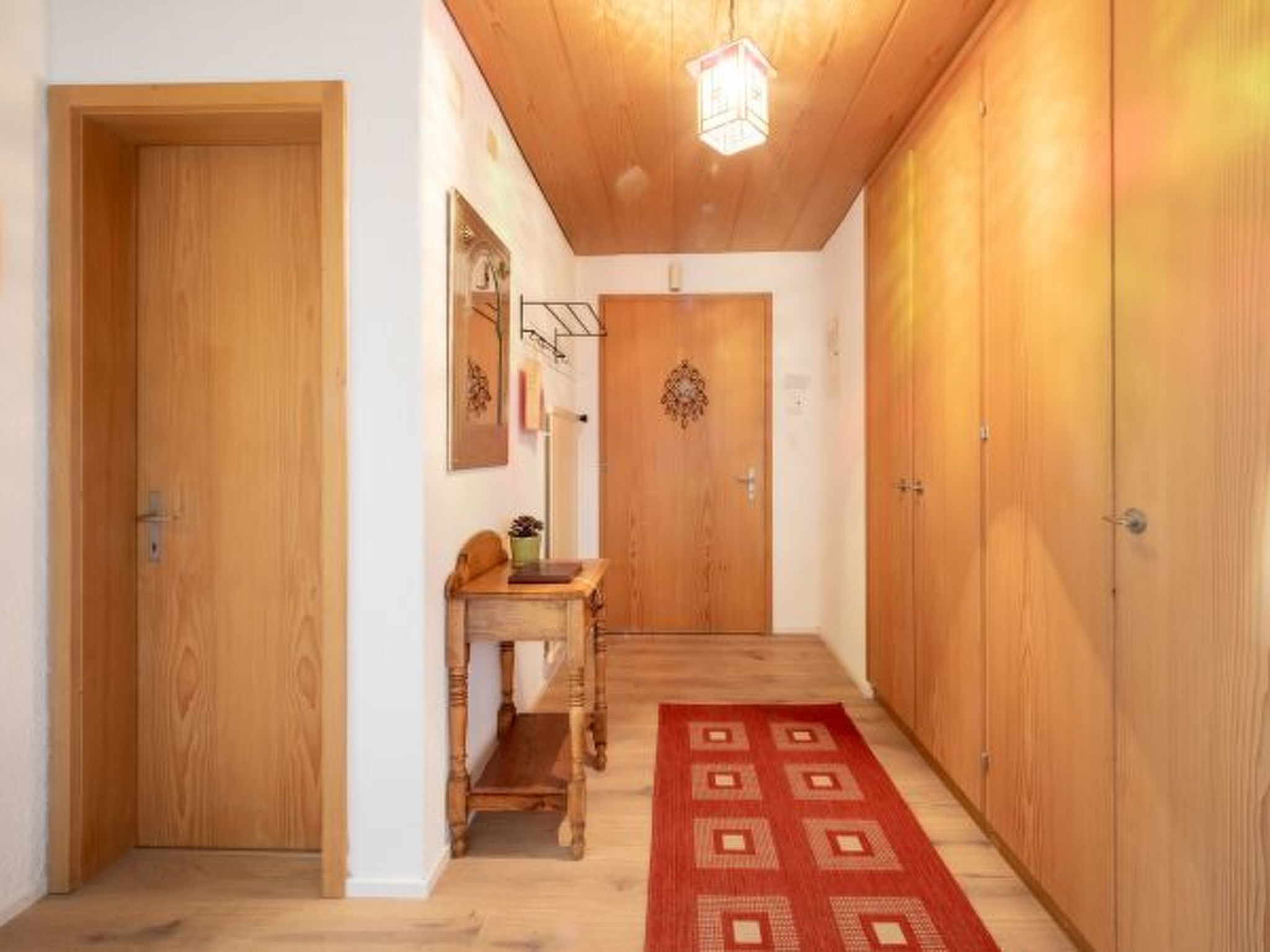Un couloir avec des portes en bois, un banc en bois, un tapis et un luminaire suspendu.