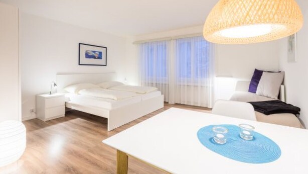 Ein modernes Hotelzimmer mit Bett, Nachttisch und einem Essbereich mit Tisch und Stühlen.