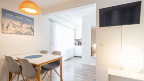 Ein moderner Essbereich mit einem Holztisch und Stühlen, einer Hängeleuchte und einem an der Wand montierten Fernseher.