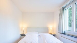 A single bed with two pillows, a nightstand with a lamp, and a window with curtains. - Cristallina A2 by Interhome (Laax)