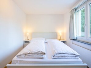 Ein Einzelbett mit zwei Kissen, ein Nachttisch mit Lampe und ein Fenster mit Vorhängen.