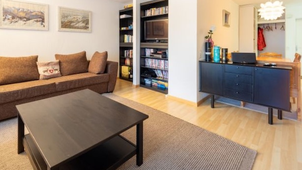 A living room with a sofa, coffee table, bookshelf, and a TV stand. - Cristallina A2 by Interhome (Laax)
