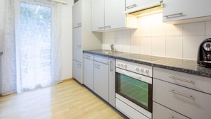 A kitchen with white cabinets, a stove, and a window with a curtain. - Cristallina A2 by Interhome (Laax)