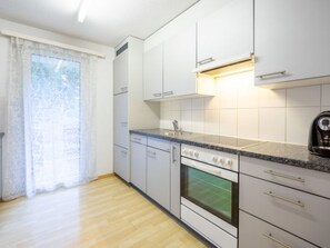 Eine Küche mit weißen Schränken, einem Herd und einem Fenster mit Vorhang.